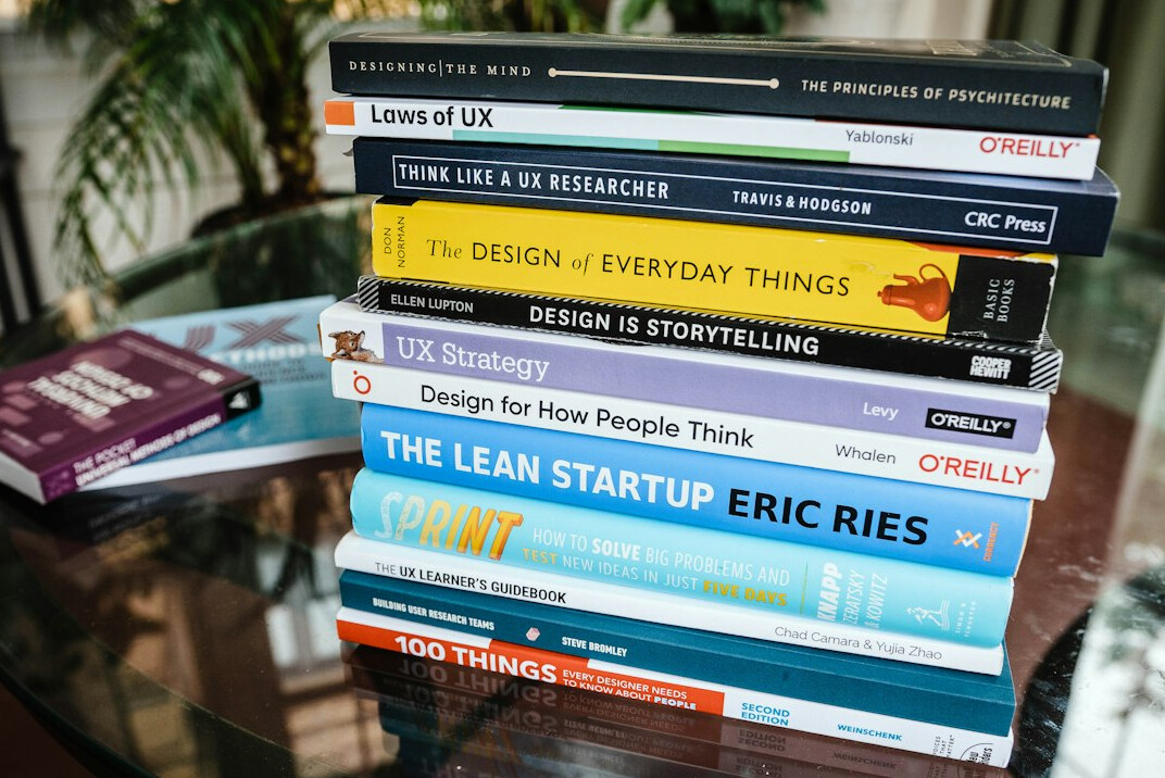 Stack of programming books on a wooden desk next to a laptop